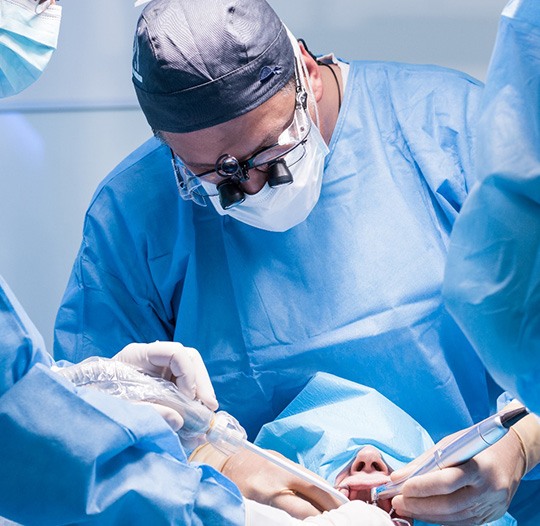 Oral surgeons in blue scrubs performing procedure on patient’s mouth