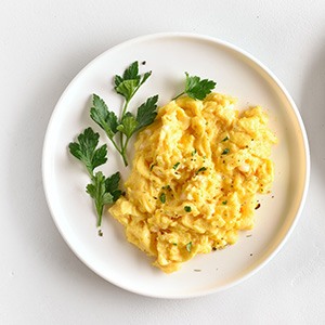 White plates with scrambled eggs and garnish on white surface