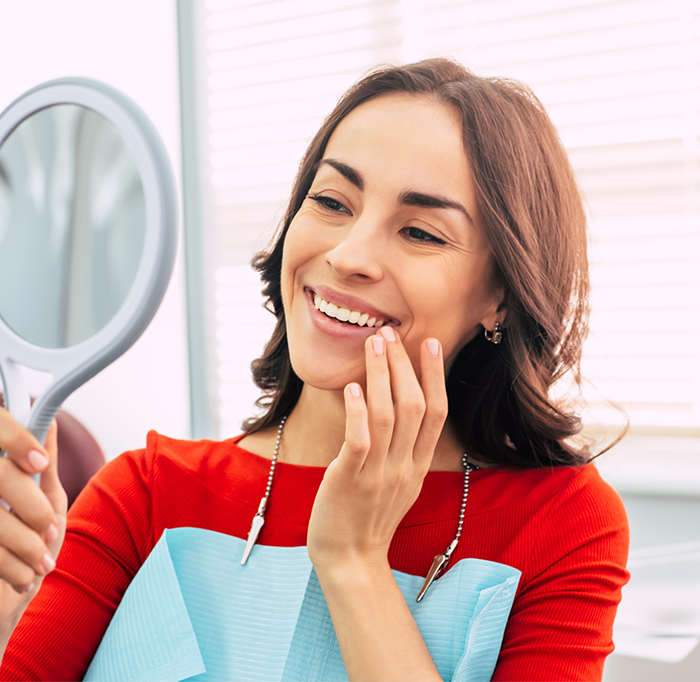 Woman in red shirt checking smile in handheld mirror