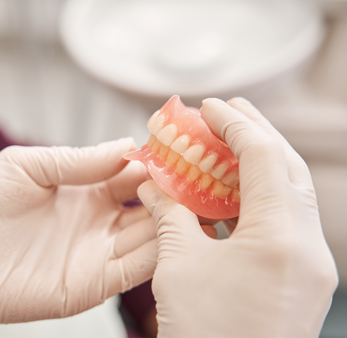 Two gloved hands holding full dentures