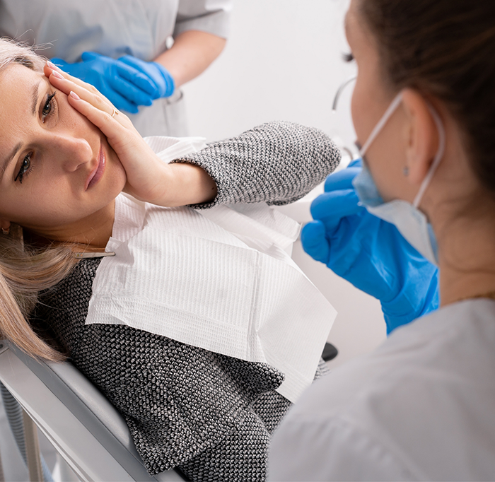 Woman in dental chair rubbing her jaw in pain